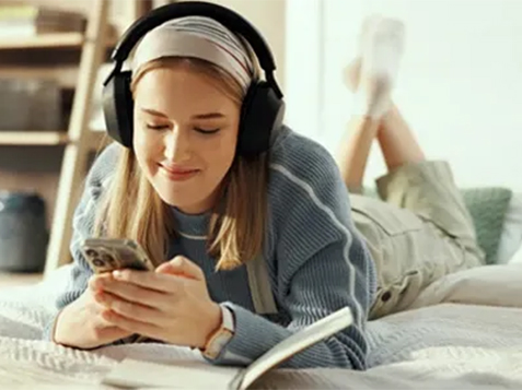 A young girl lying on her belly on a bed checking her phone