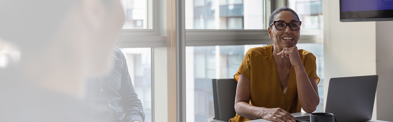 A lady sitting at a table with an open tablet, her chin resting on her fist, smiling and looking ahead
