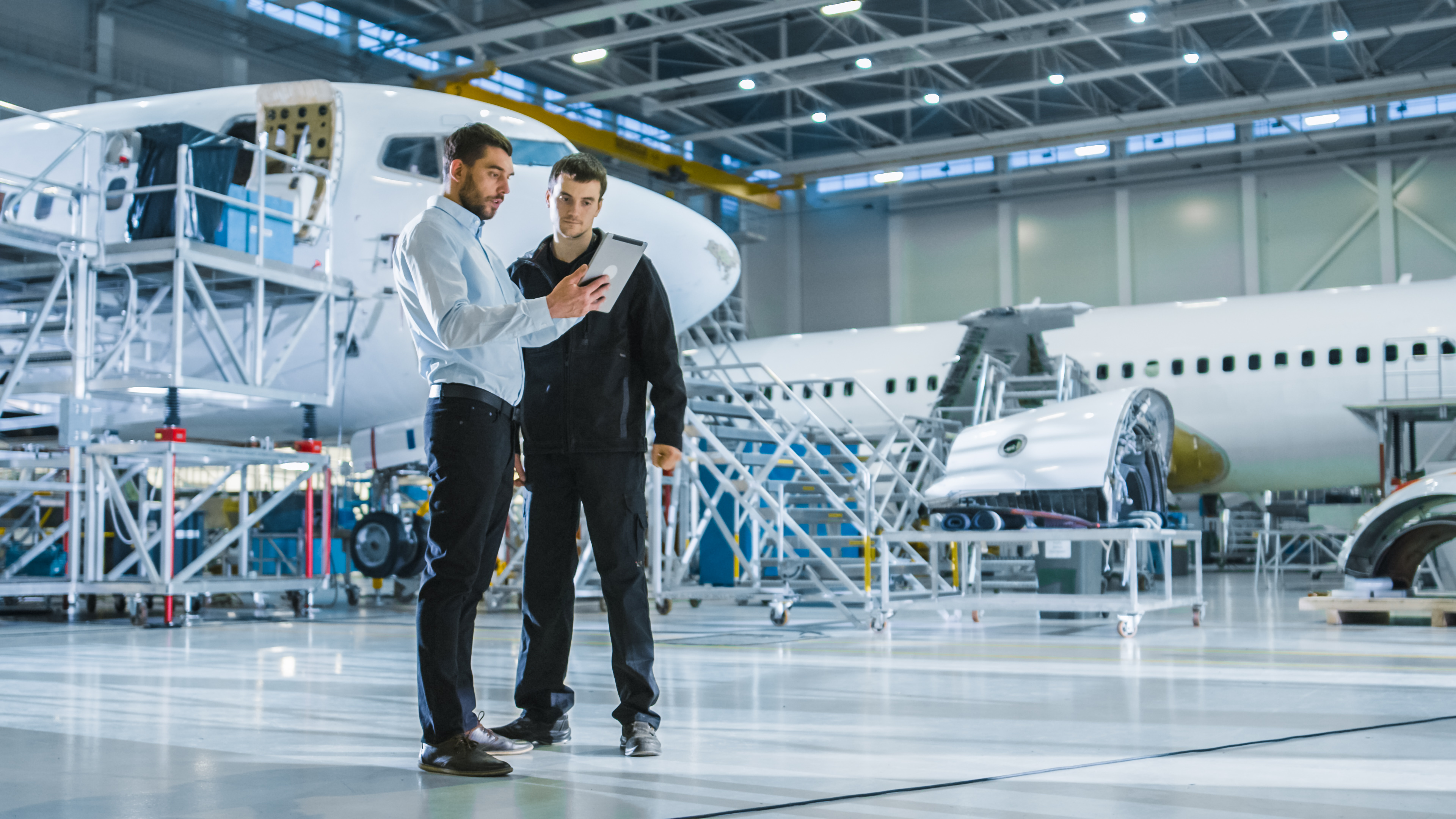 A personnel showing a tablet to another aircraft worker and explaining something in a hangar
